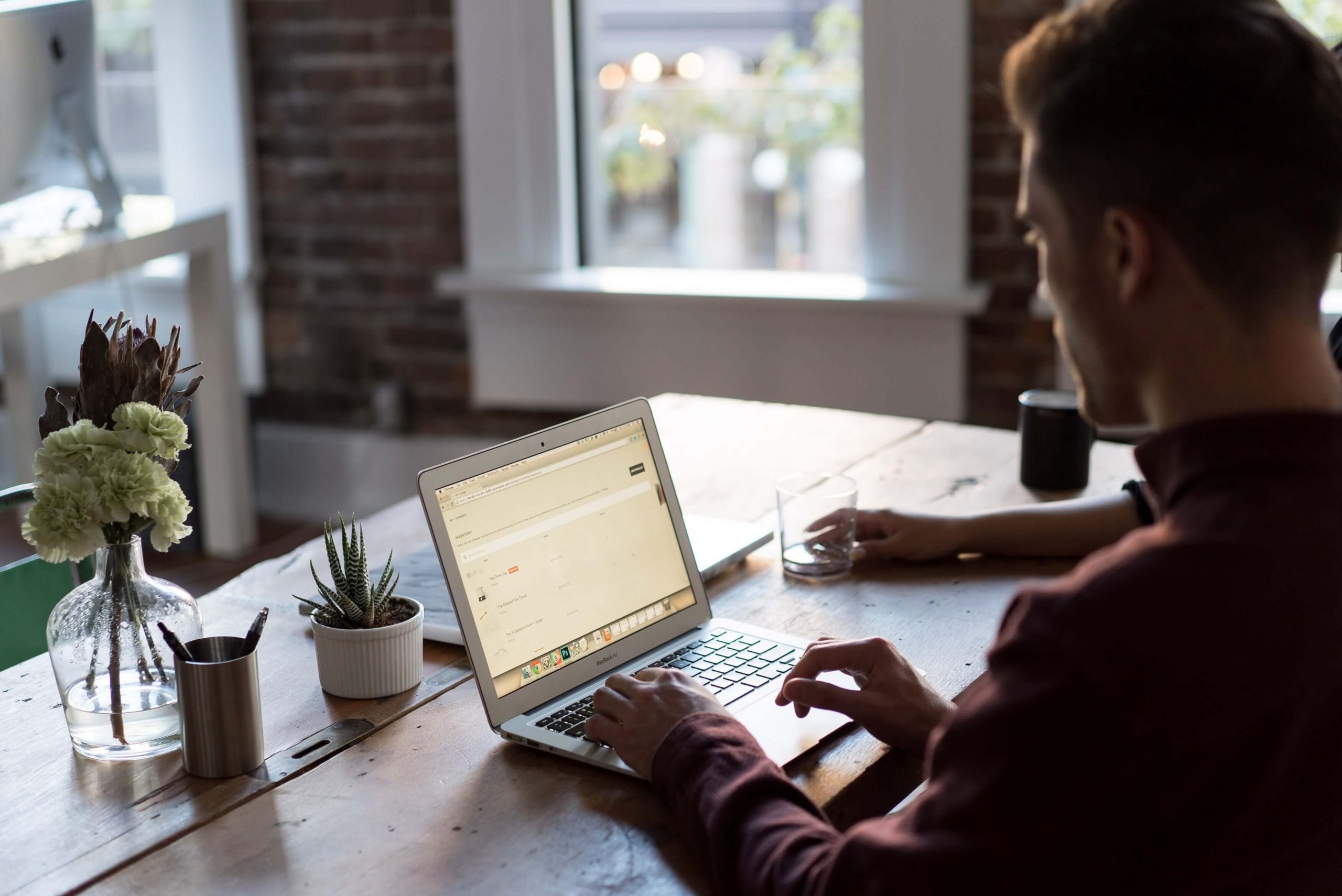 Jovem concentrado usando um notebook em um ambiente moderno, trabalhando ou navegando na internet, com iluminação aconchegante e uma xícara de café ao lado